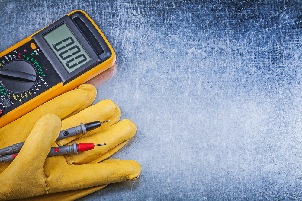 A pair of yellow gloves next to a digital multimeter.